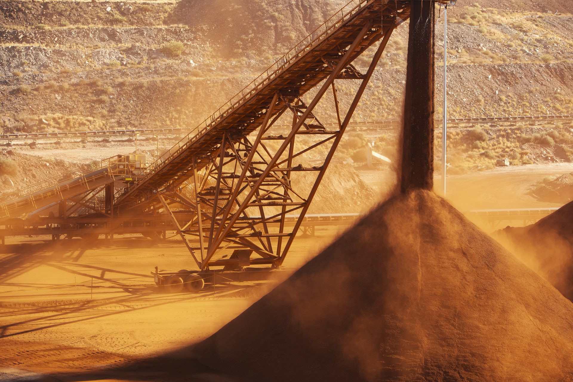 Stacker conveyor dropping bulk ore onto a stockpile, with dust rising from the pile